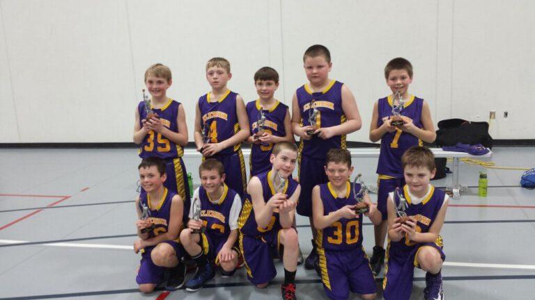 A youth basketball team posing with trophies in a gym.